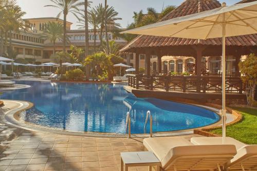 a pool at a resort with chairs and an umbrella at Secrets Bahía Real Resort & Spa Adults only in Corralejo