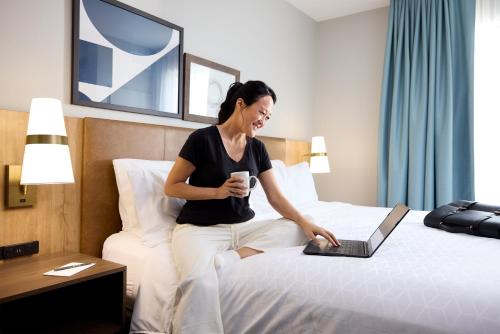 a woman sitting on a bed with a laptop at Staybridge Suites Columbia - Baltimore by IHG in Columbia