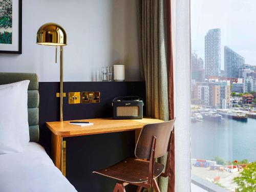ロンドンにあるTRIBE London Canary Wharfのデスク、ベッド、窓が備わるホテルルームです。
