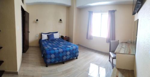 a bedroom with a bed with a blue comforter and a window at Hotel Sevilla in Guatemala