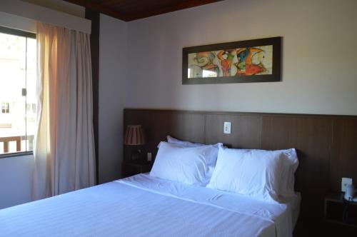 a bedroom with a bed with white sheets and a window at Pousada Terê Parque in Teresópolis