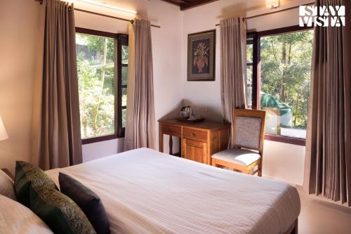 a bedroom with a bed and a desk and windows at StayVista at Vale Echoes - Breakfast Included in Munnar
