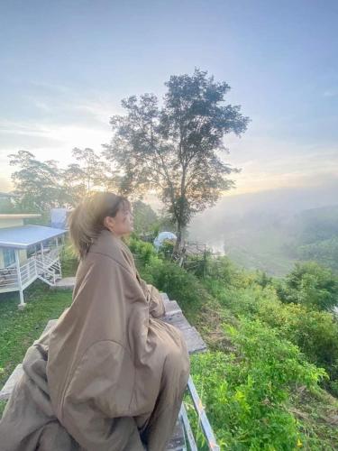 a woman sitting on a bench looking at the view at Doi Sang Farm Stay - ดอยซางฟาร์มสเตย์ in Ban Huai Kom