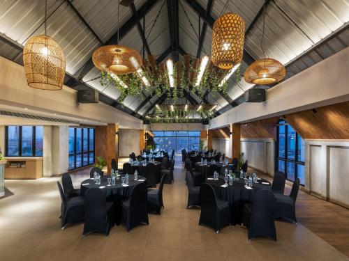 ジョグジャカルタにあるAveta Hotel Malioboroの黒いテーブルと椅子、シャンデリアが備わる宴会場