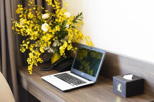 a laptop computer on a desk with a vase of yellow flowers at Daphovina Hotel in Nha Trang
