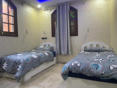 a bedroom with two beds and two windows at Riad Targante Takate 1 in Sidi Bibi