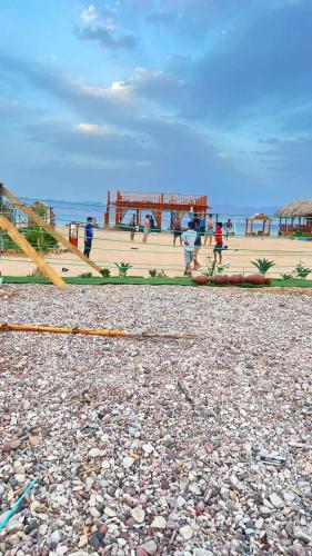 people walking on a beach with a pier in the background at Green Beach Camp & Hotel in Nuweiba