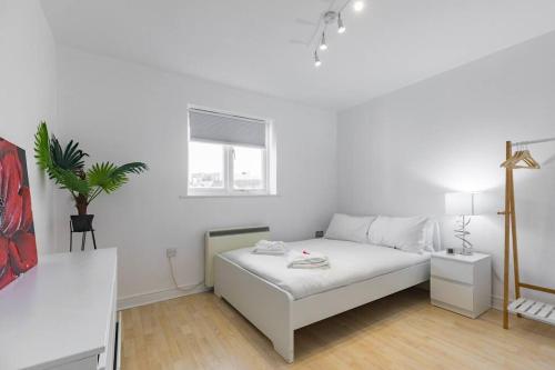 una camera bianca con un letto bianco e una pianta di 2-BR London Oasis in Woolwich a Londra