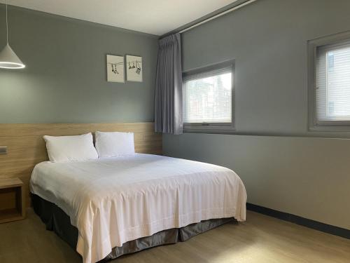 a bedroom with a bed with white sheets and two windows at Prince Hotel in Jiaoxi