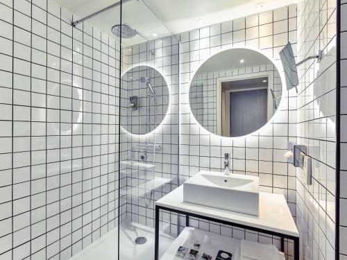 La salle de bains est pourvue de carrelage blanc, d'un lavabo et d'un miroir. dans l'établissement Mercure Paris la Défense Grande Arche, à Nanterre