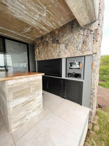 cocina con armarios negros y pared de piedra en Casa en la montaña en Villa del Dique