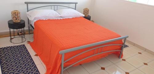 een bed met een oranje deken en witte kussens bij COSY Tamarins 2 plage à quelques mètres à pied in Sainte-Anne