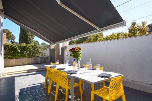 卡里勒魯埃的住宿－La Maison de la Plage du Rouet，一张餐桌,上面有黄色的椅子,放在黑伞下