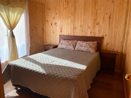 Un dormitorio con una cama con paredes de madera y una ventana en Cabaña Llonquén, en Liquiñe
