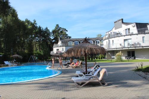 a resort with a swimming pool with chairs and an umbrella at Sunny Adventure Baltic Apartament in Pobierowo