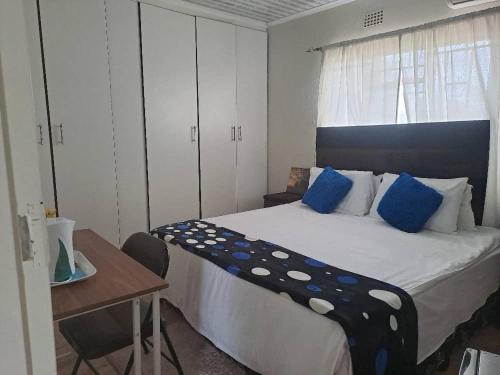 Schlafzimmer mit einem Bett mit blauen Kissen und einem Schreibtisch in der Unterkunft Virgin guesthouse in Francistown