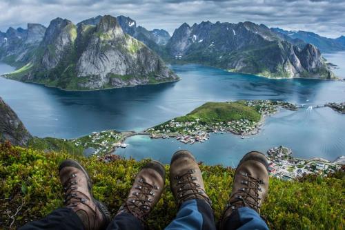 a person sitting on top of a mountain overlooking a body of water at Reine Front View - Mountain & Seaview in Reine