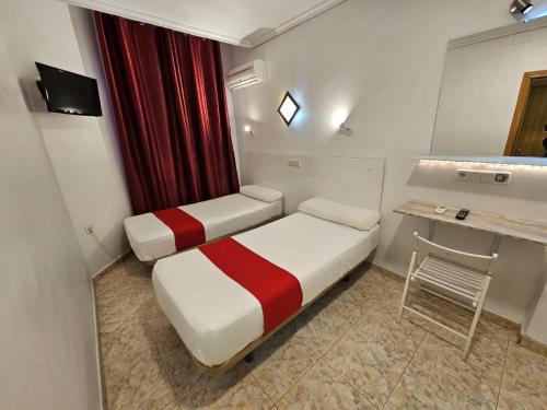 Habitación pequeña con 2 camas, mesa y escritorio. en Hostal Las Vegas, en Madrid