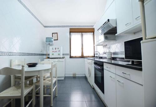 una cocina con armarios blancos, una mesa, una mesa y un tocador en APARTAMENTO EN CANDAS, en Candás