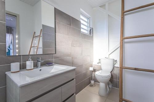 a white bathroom with a sink and a toilet at Magnifique Bungalow et Jacuzzi au cœur des plages in Le Moule