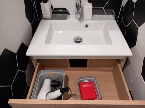 a bathroom sink with a white counter and a red container at La cour fleurie, tout confort in Dijon