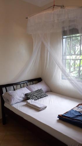 a bed with a white canopy and a window at Mini Lookout Entebbe in Entebbe