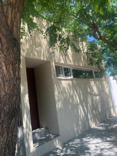 un bâtiment blanc avec une porte à côté d'un arbre dans l'établissement Las Tipas mini loft Cafayate, à Cafayate