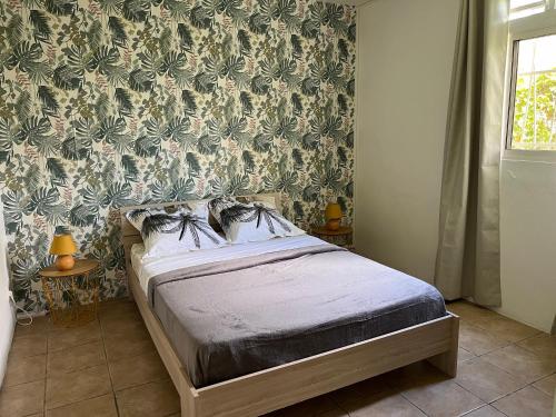 - une chambre avec un lit et un mur orné d'un papier peint floral dans l'établissement chaleureux bas de villa vue mer, à Fort-de-France
