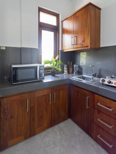 a kitchen with wooden cabinets and a microwave at Villa Windfall Unawatuna in Unawatuna