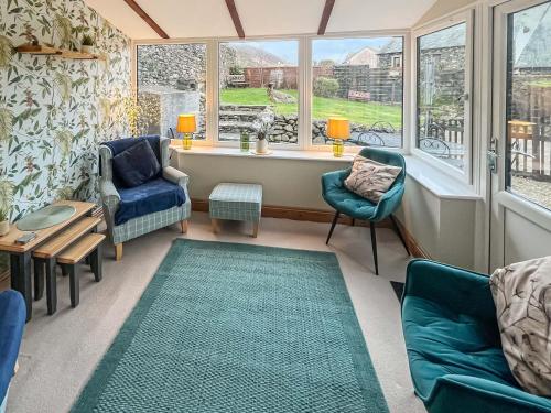 a living room with chairs and a table and windows at Apple Tree Cottage in Threlkeld