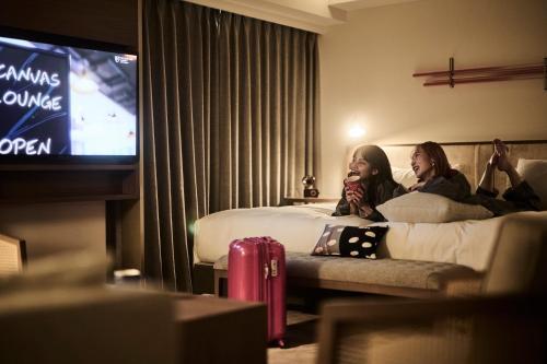 two women sitting on a bed watching a tv at The Royal Park Canvas - Kyoto Nijo in Kyoto