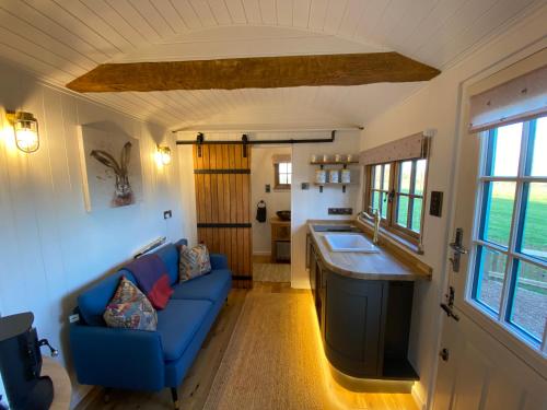 a living room with a blue couch and a kitchen at Luxury Shepherd Hut in Kelham