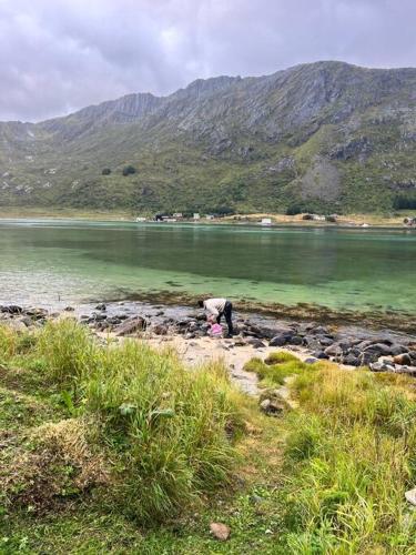 a person standing on the shore of a body of water at Lofoten Fjord Apartment - Kvalvika Beach & Ryten in Skjelfjord
