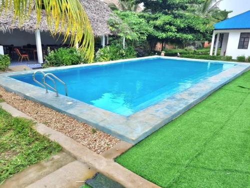 a swimming pool in a yard with a green lawn at Kigwedeni Villas in Nungwi