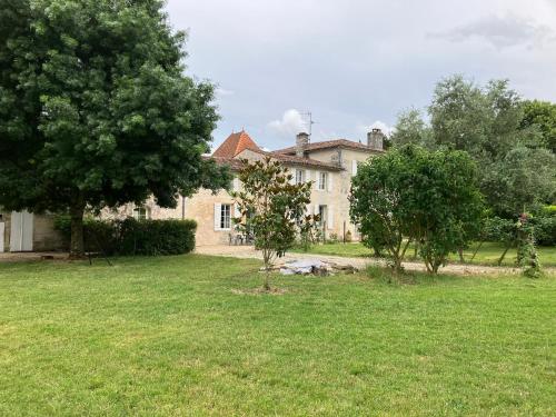 une grande maison avec des arbres devant une cour dans l'établissement Gite des Noisettes à la porte de Saintes, à Chermignac