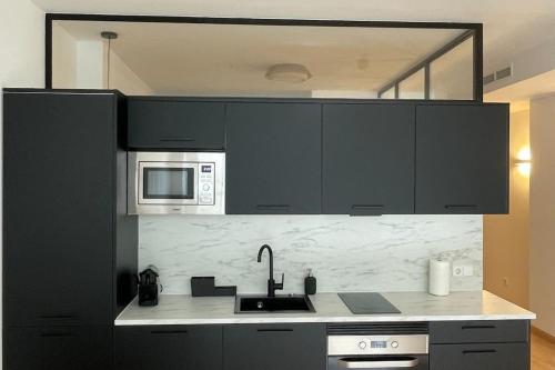 a kitchen with black cabinets and a sink and microwave at Soho Moraleja III in Alcobendas