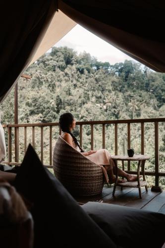 a woman sitting in a chair on a porch looking out at the mountains at Glamping tent in Pelaga Eco Park in Patjung