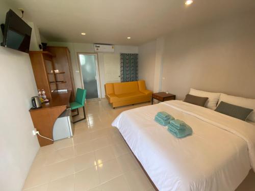 um quarto com uma cama branca e um sofá amarelo em Aiyapach Inn em Chon Buri