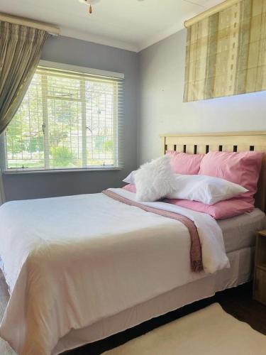 a bedroom with a large bed with pink and white pillows at The M-Pire Cottage in Bloemfontein