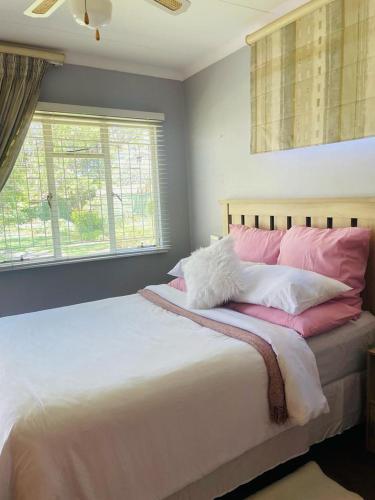 a bedroom with a large bed with pink and white pillows at The M-Pire Cottage in Bloemfontein