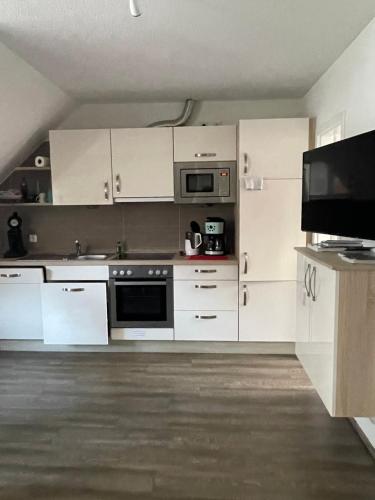 Haus Julianne, Wohnung Backbord, Familie Poppinga في نورديرني: مطبخ مع دواليب بيضاء وتلفزيون بشاشة مسطحة
