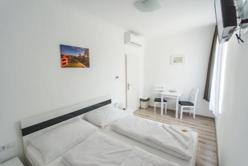 a white bedroom with a bed and a table at BL Garden Panzió in Balatonlelle