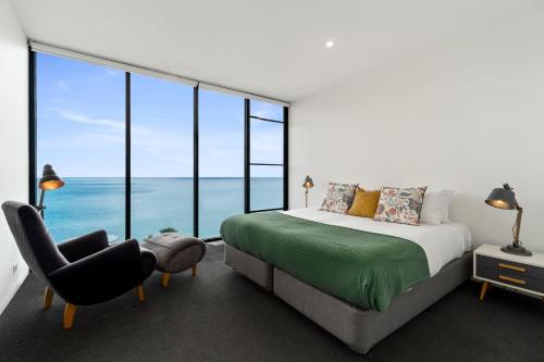a bedroom with a bed and a chair and large windows at Cape Wye in Wye River