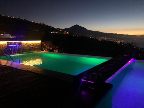 a swimming pool with green and purple lighting at night at Apartamento Teide Piscina Climatizada in Sauzal