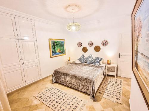 a white bedroom with a bed and a chandelier at Le Superbe - Sidi Bou Saïd in Dar Mimoun Bey