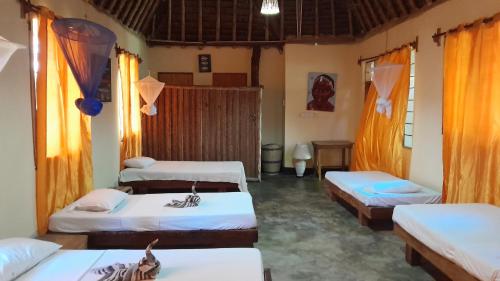 Habitación con 3 camas y cortinas de color naranja. en Ushongo Beach Bandas, en Pangani