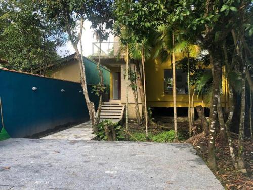 uma casa amarela com uma cerca azul e árvores em Sobrado c/ PISCINA na Barra do Una (Litoral Norte) em São Sebastião