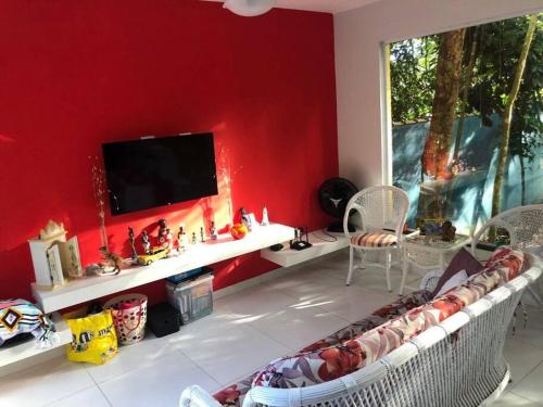 ein Wohnzimmer mit einer roten Wand und einem TV in der Unterkunft Sobrado c/ PISCINA na Barra do Una (Litoral Norte) in São Sebastião
