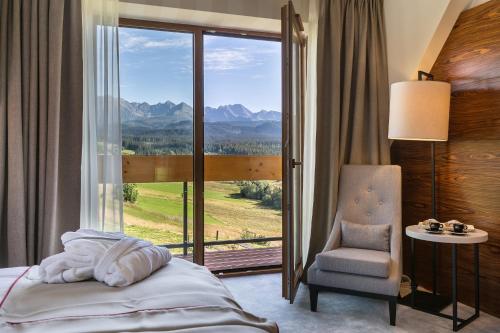 a bedroom with a bed and a chair and a window at Hotel Kopieniec Fizjo- Med & SPA in Murzasichle