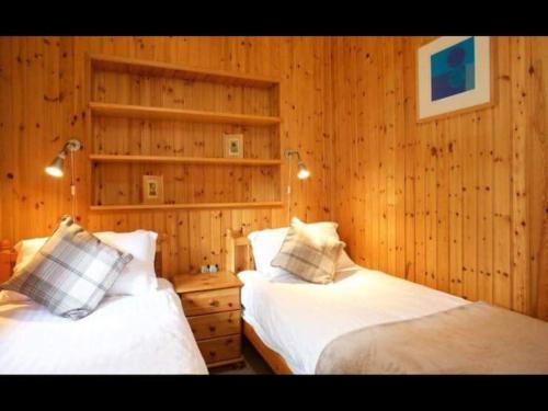 two beds in a room with wooden walls at The Crannog on Loch Tay in Morenish